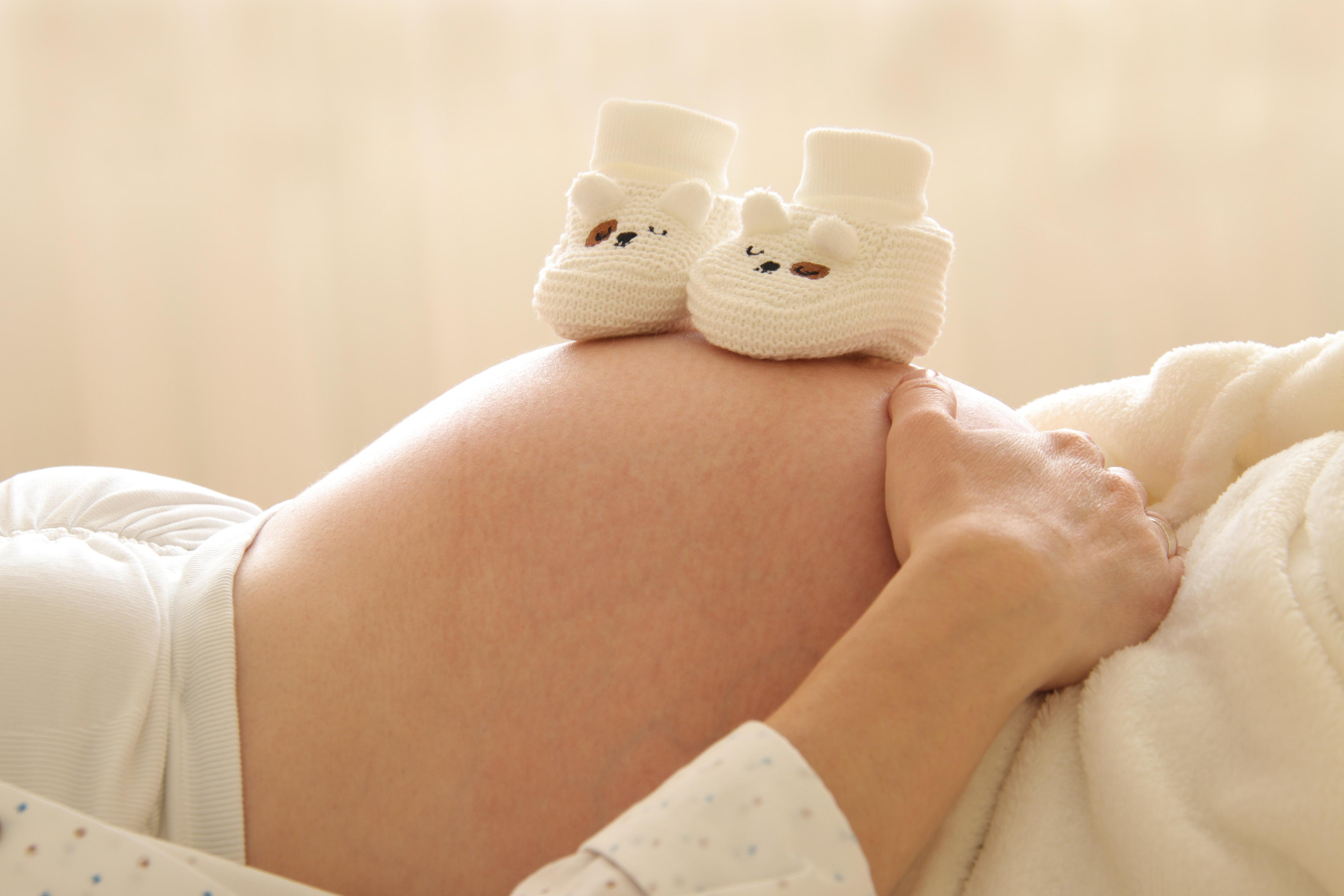 Femme enceinte avec chaussons de bébé sur son ventre, attente de la naissance et maternité